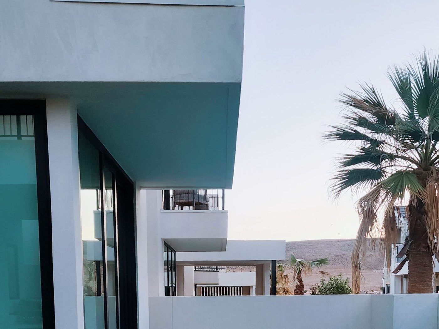 Reference image: a white rendered house with deep cantilevered shade overhangs and a covered balcony, desert hills behind