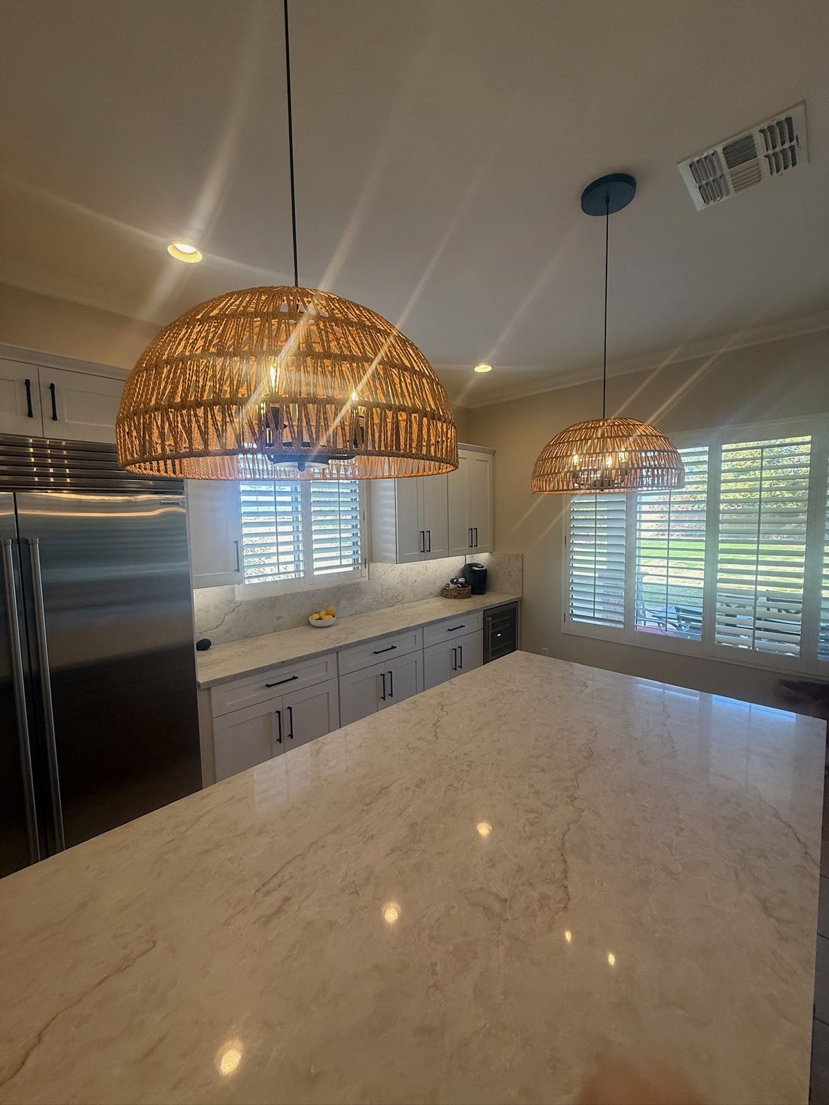 Stanley Brothers project: a stone island lit by woven pendants with shutters and a built-in refrigerator behind