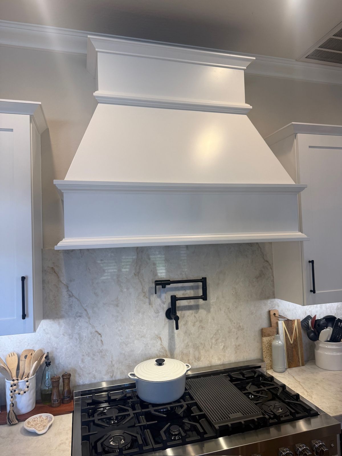Stanley Brothers project: a painted custom range hood above a marble slab backsplash with a pot filler